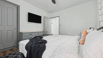 A bedroom with a bed, a ceiling fan, a dresser, and a television.