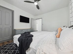 Un dormitorio con cama, ventilador de techo, cómoda y televisor.