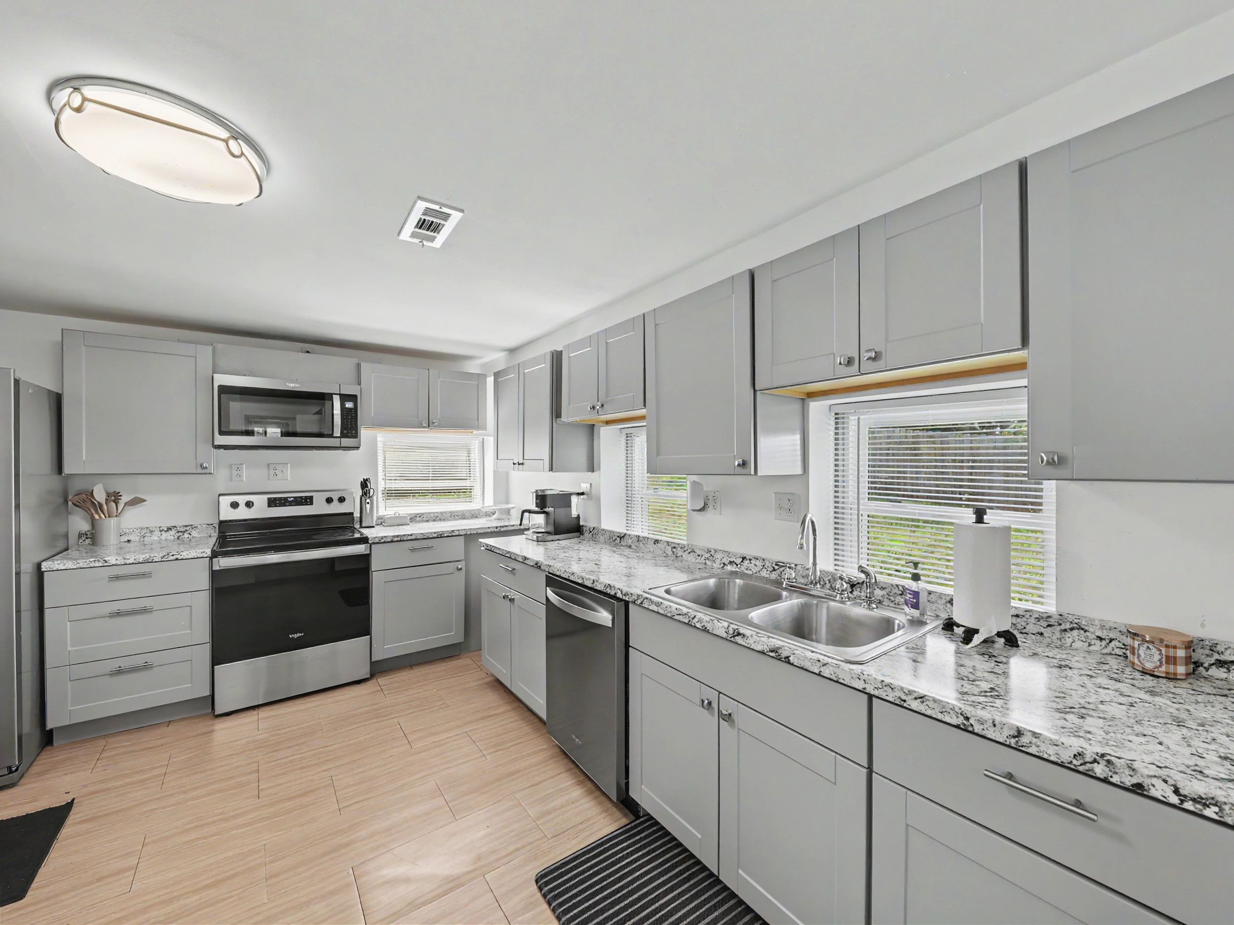 A modern kitchen with grey cabinets, stainless steel appliances, a granite countertop, and a window with blinds.