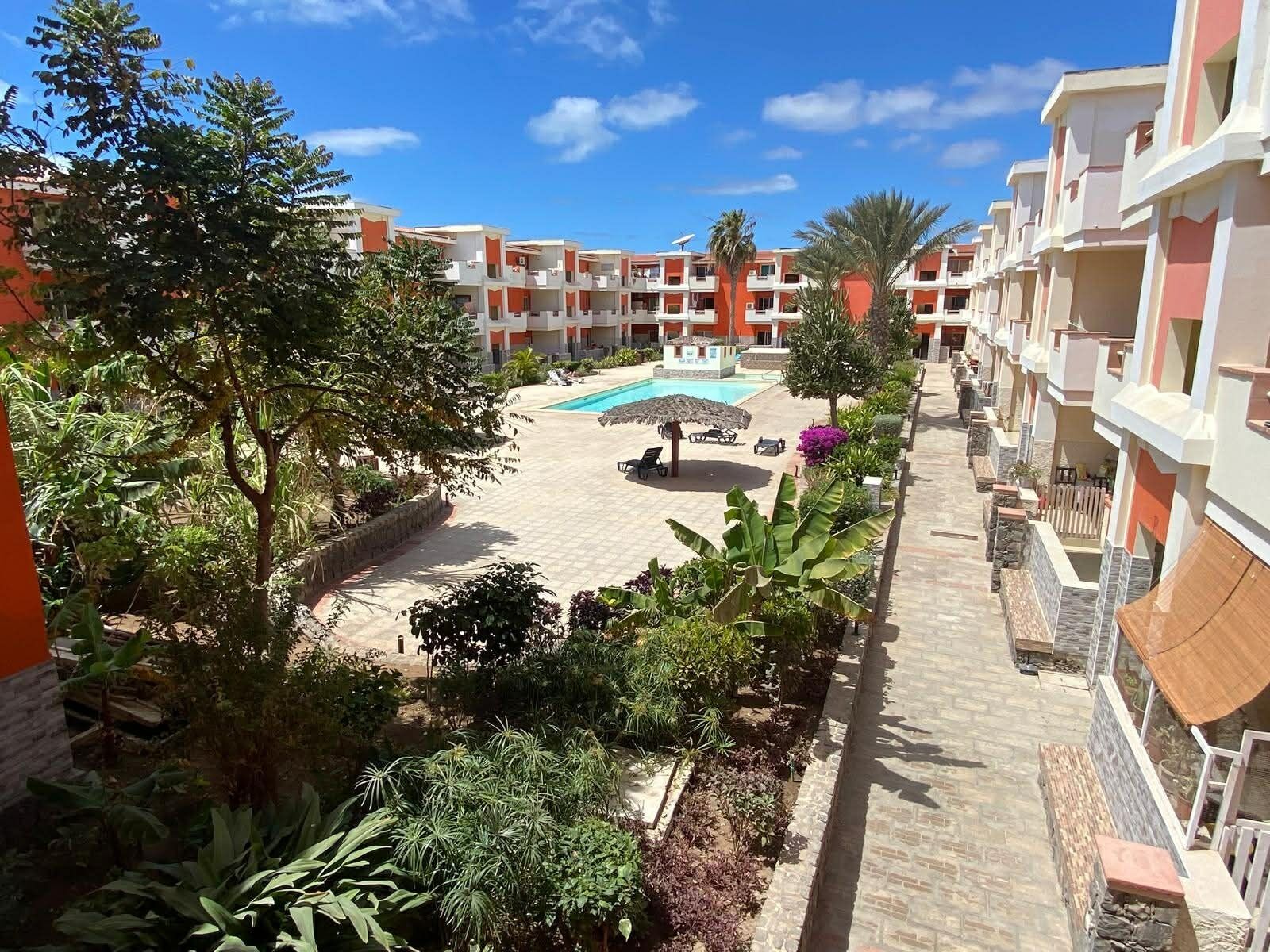 A hotel courtyard with a swimming pool, lounge chairs, and a variety of plants.
