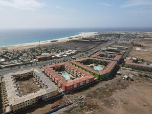 A coastal hotel complex with multiple buildings, a swimming pool, and a beach in the background. - Peaceful 2-bedroom apartment with AC in Santa Maria. 400m from the beach. (Santa Maria)