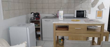 Cocina compacta con refrigerador, microondas, cafetera y una pequeña mesa de comedor con sillas.