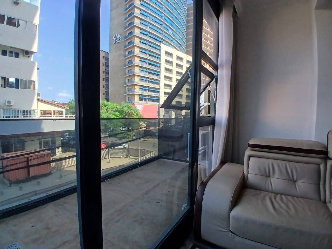 Ein Balkon mit Blick auf eine Stadtlandschaft, darunter ein hohes Gebäude mit blauer Fassade.