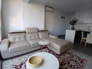 A modern living room with a beige sectional sofa, a small white coffee table, and a patterned rug. - Casa Bella (Maputo)