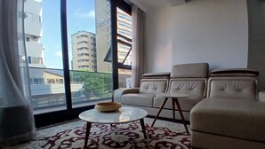 Un salon avec un canapé, une table basse et une vue sur les immeubles à travers de grandes fenêtres.