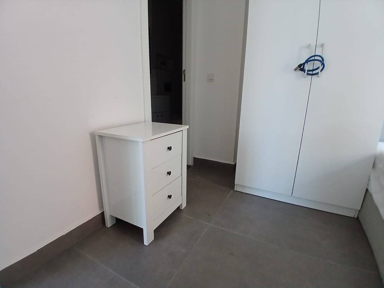 Een kamer met een witte nachtkastje met lades en een garderobe met een deurklink.