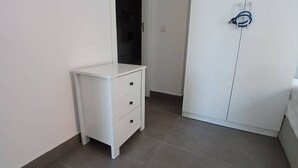 Une chambre avec une table de chevet blanche dotée de tiroirs et une armoire avec une poignée de porte.