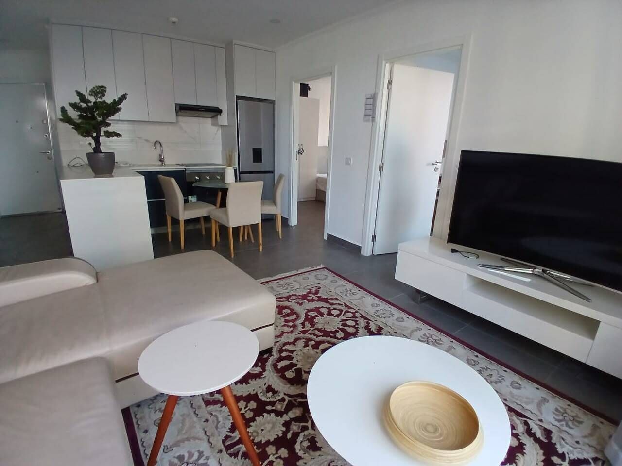 Una sala moderna con un sofá, una mesa de centro, un televisor y una cocina al fondo.