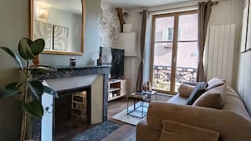 Een gezellige woonkamer met een open haard, een bank, een grote spiegel en uitzicht op buiten.