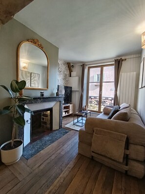 A cozy living room with a fireplace, a sofa, a large mirror, and a view of the outside. - Vrbo Property (Chartres)