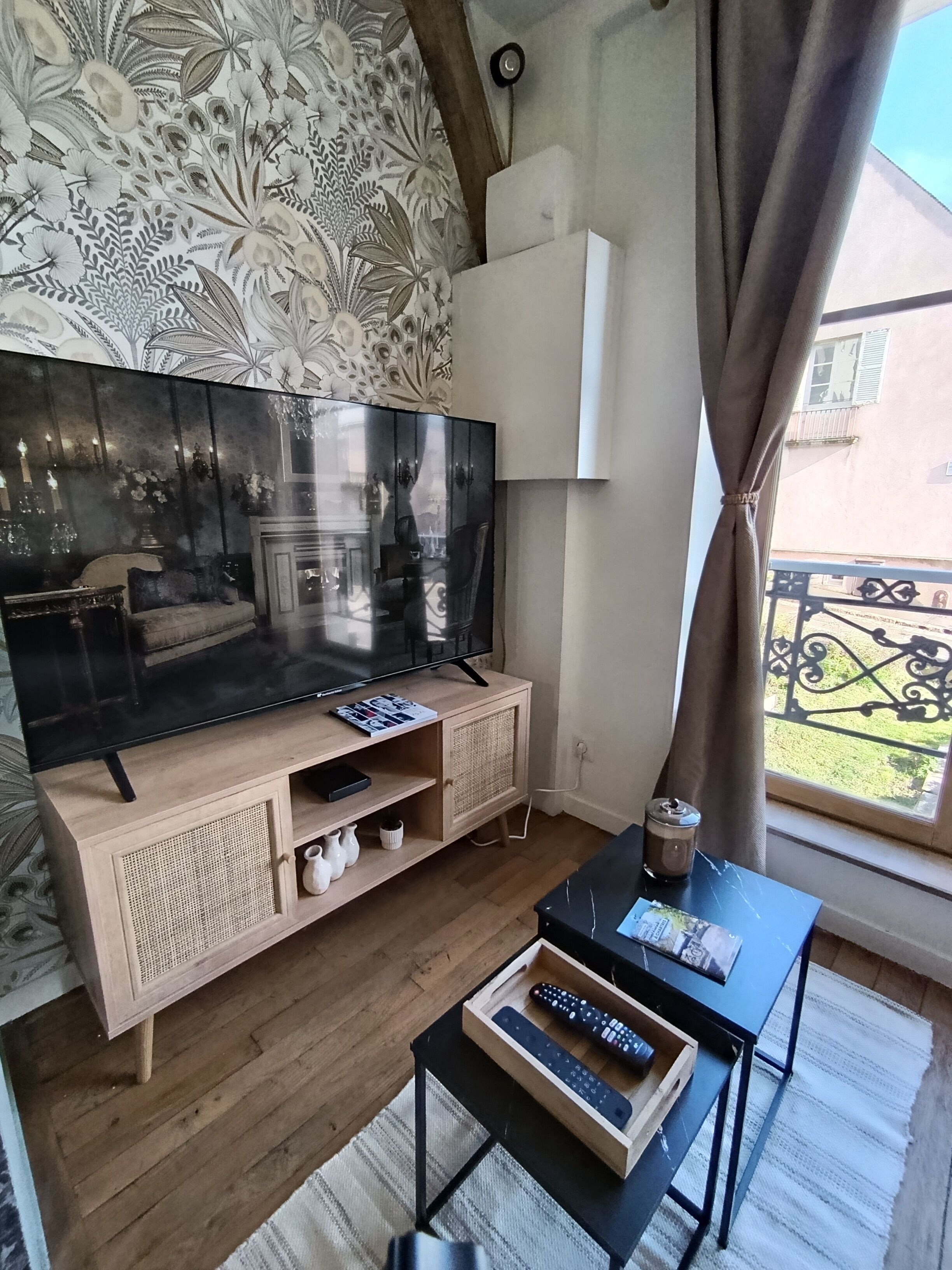 En stue med et stort fladskærms-tv, en tv-reol i træ og et lille bord med fjernbetjeninger.