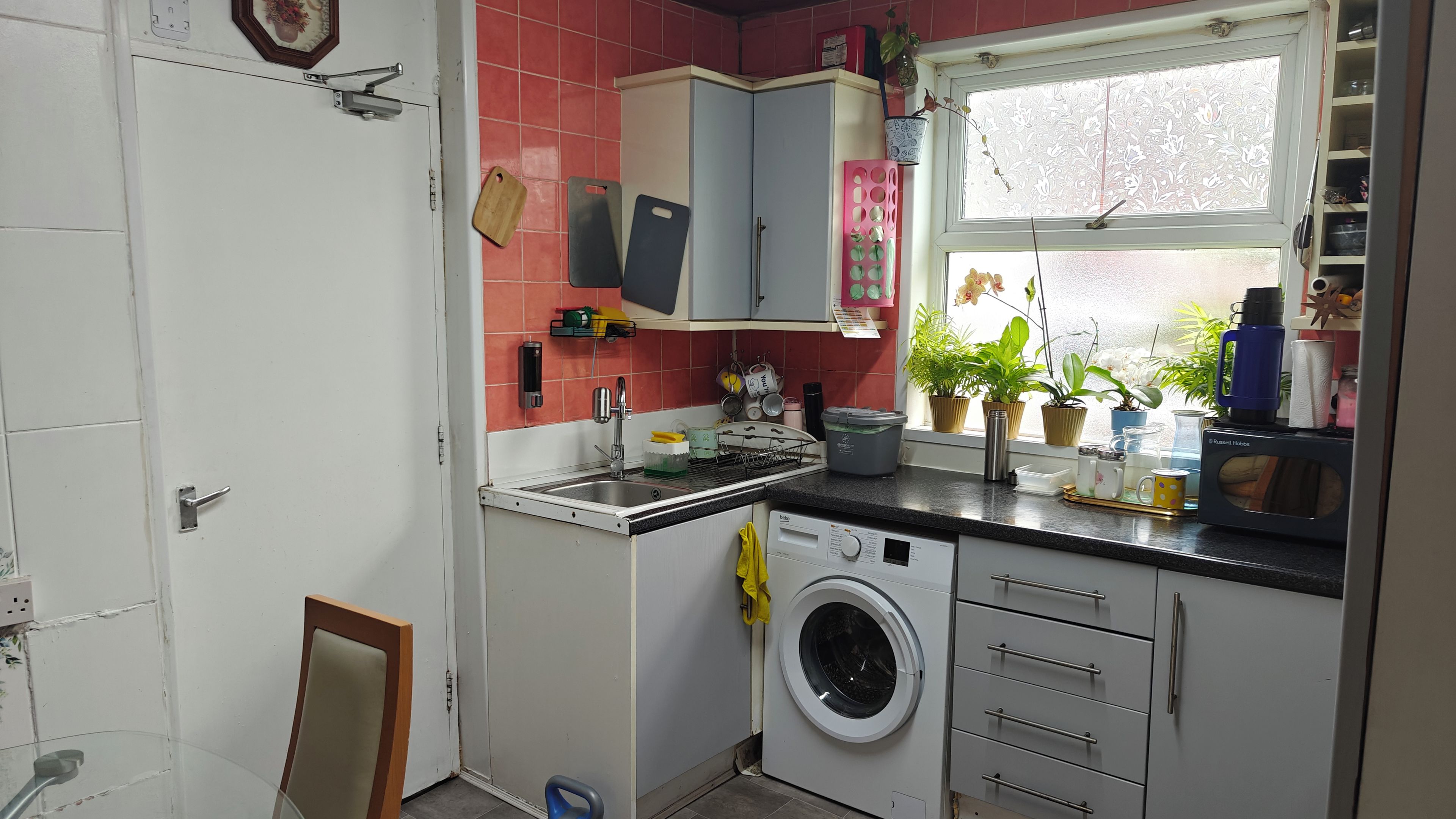 Una cocina compacta con lavadora, un lavamanos y una ventana con plantas en macetas.