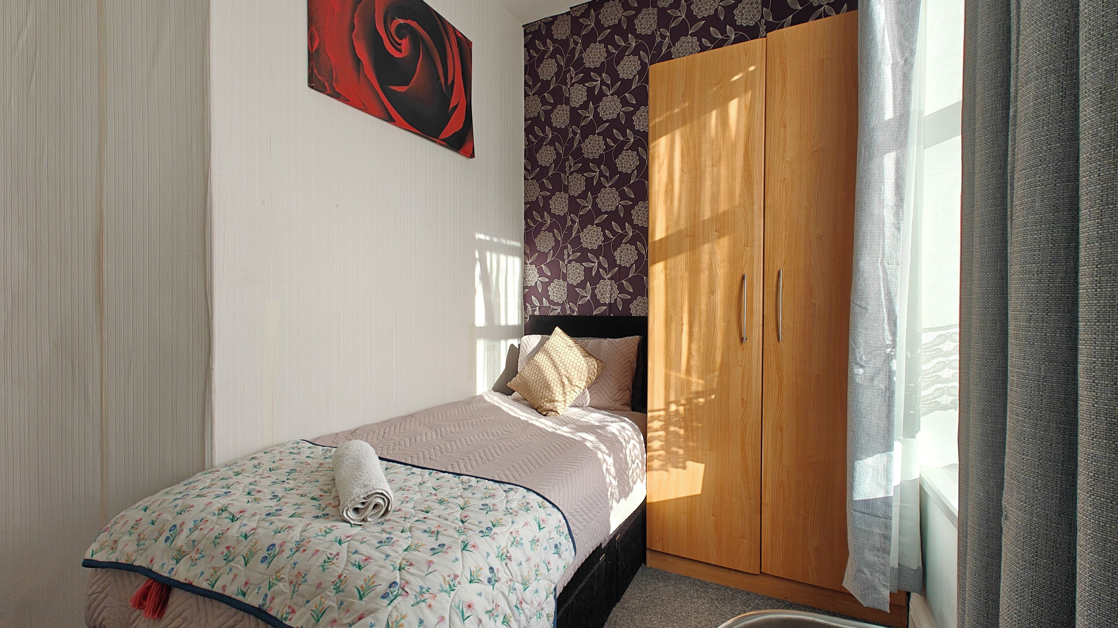 A bedroom with a bed, a wardrobe, and a window with curtains.