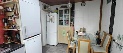 Une cuisine compacte avec des meubles blancs, un réfrigérateur, une table à manger avec des chaises et un lustre.