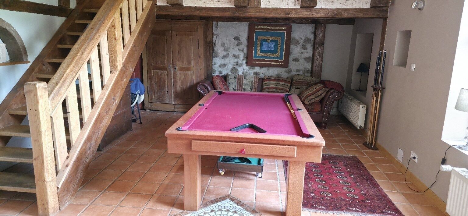 Een pooltafel in een kamer met een houten trap, een vloerkleed met patroon en een lijst met een afbeelding aan de muur.
