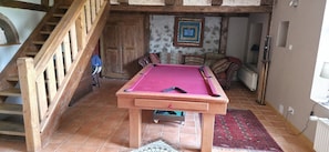 A pool table in a room with a wooden staircase, a patterned rug, and a framed picture on the wall. - Domaine du Rouhu (Fouchy)