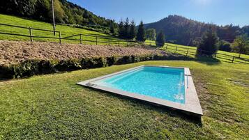 A rectangular swimming pool with a clear blue water surface, surrounded by a well-maintained grassy area and a wooden fence.