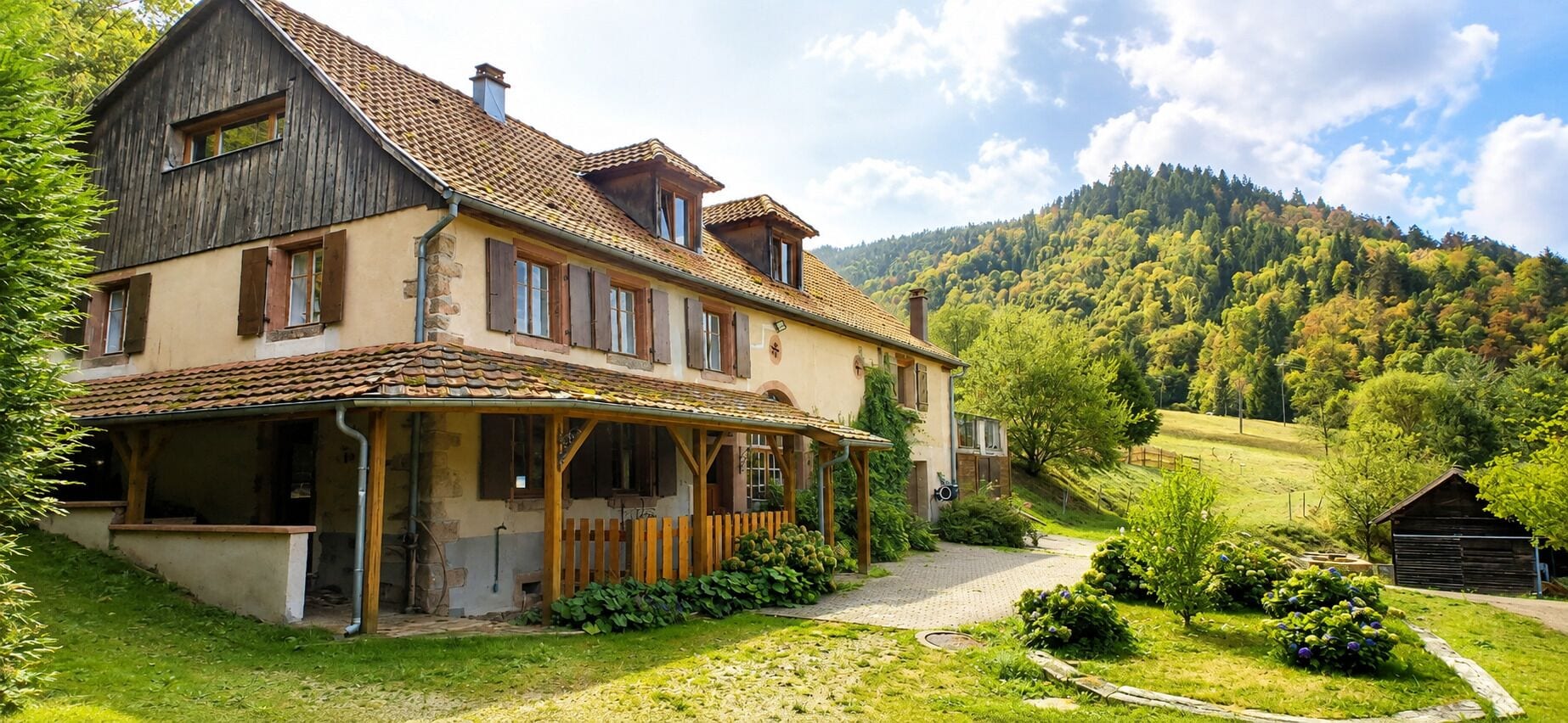 A two-story house with a covered porch, a stone chimney, and a hillside view.