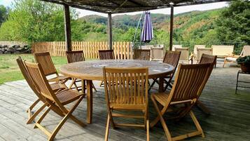 An outdoor wooden deck with a round table and chairs, surrounded by a wooden fence, overlooking a hilly landscape.
