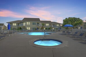 Ein Poolbereich mit zwei runden Pools, Liegestühlen und einem Gebäude mit Balkonen im Hintergrund.