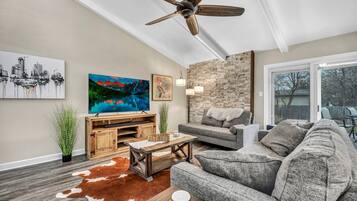 A living room with a ceiling fan, a large painting, a stone wall, a gray sofa, and a wooden coffee table.