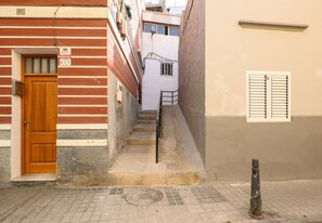 Uma passagem estreita com uma porta de madeira e um corrimão de metal que dá para uma escadaria.
