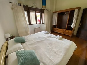 Ein Hotelzimmer mit Bett, Holzschrank, Fenster mit Vorhängen und Heizkörper.