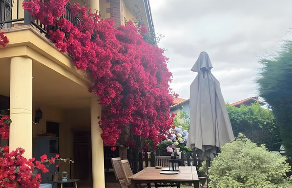 A balcony with red flowering plants, a table with chairs, and a grey umbrella. - House with Garden Steps from Cantabria’s Main Beaches (Arguedes)