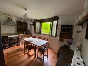 A kitchen with a dining table, chairs, a clock, and a window with a view of greenery. - House with Garden Steps from Cantabria’s Main Beaches (Arguedes)
