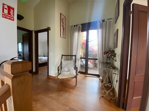 A hotel room with a wooden floor, a bed, a chair, a balcony with curtains, and a desk with a lamp. - House with Garden Steps from Cantabria’s Main Beaches (Arguedes)