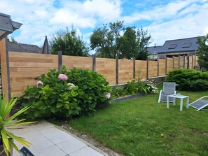 A backyard with a wooden fence, green shrubs, a small garden bed, and outdoor furniture. - House 'La Rue, Petite Maison de Pêcheur proche plage' (Cancale)