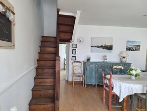 A staircase leading to a dining area with a wooden table and chairs, a blue cabinet, and wall-mounted artwork. - House 'La Rue, Petite Maison de Pêcheur proche plage' (Cancale)