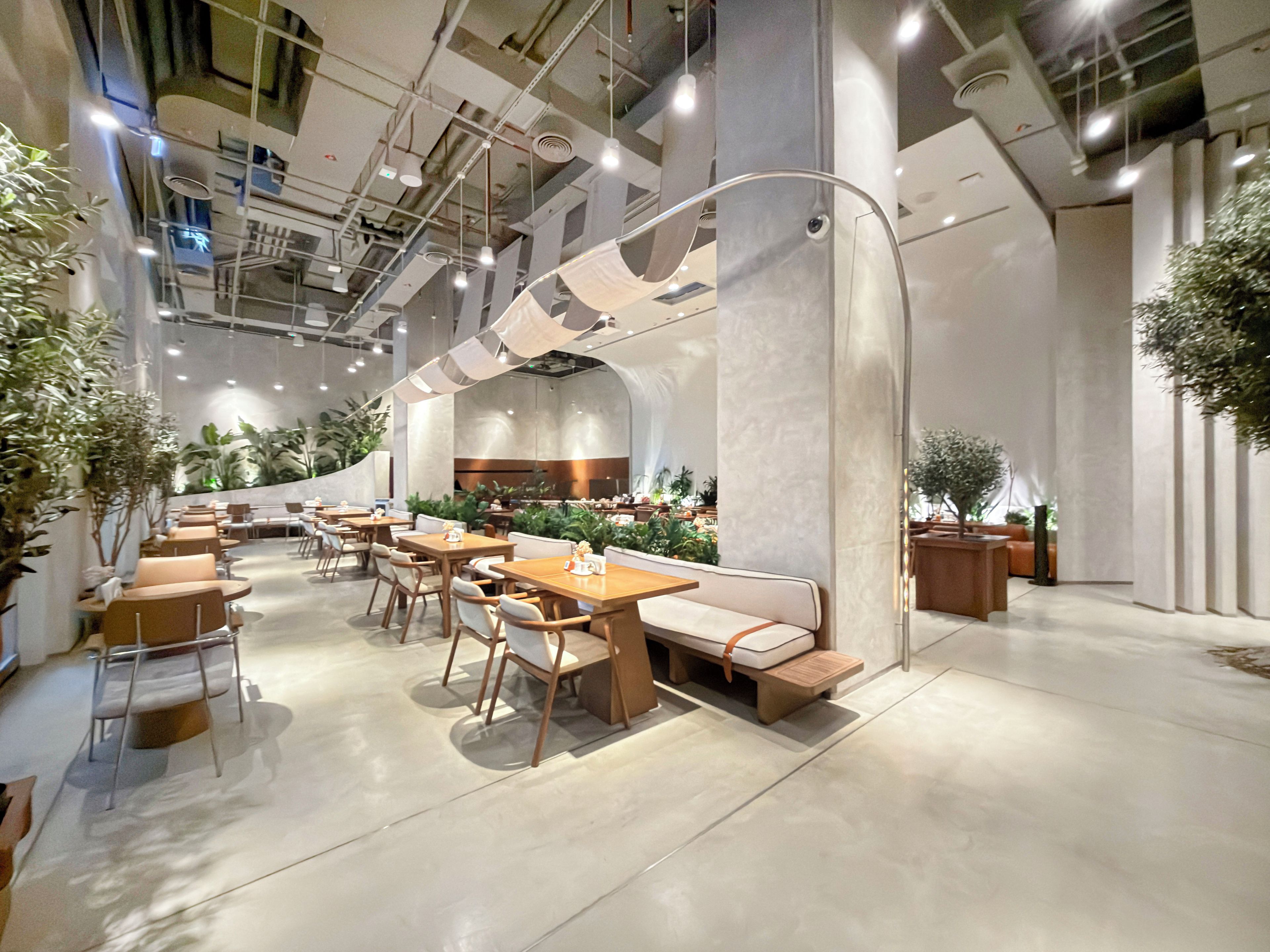 Ein modernes Interieur mit Tischen und Stühlen, die zum Essen angerichtet sind, einer gebogenen Bank und Zimmerpflanzen.