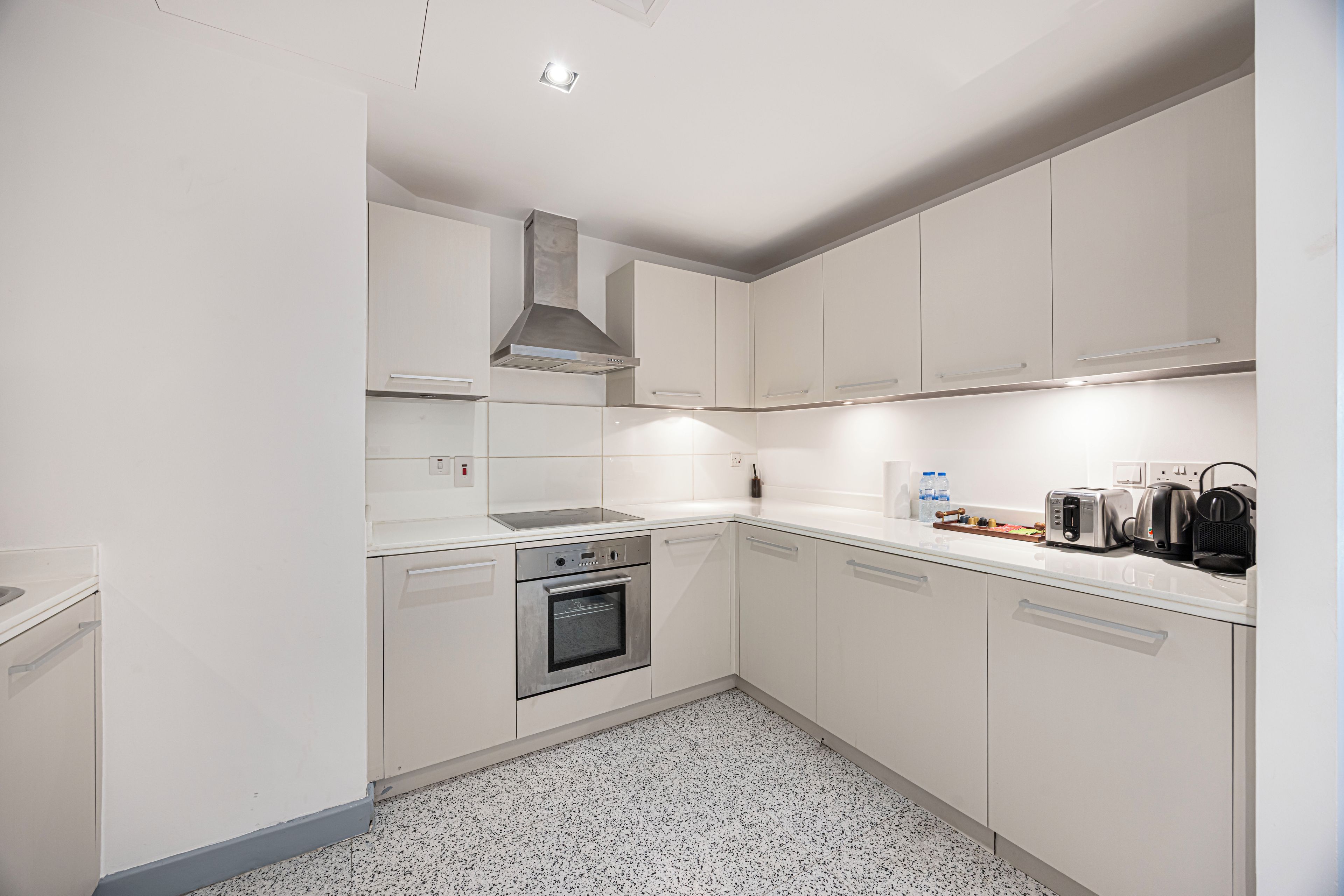 Een moderne keuken met witte kasten, roestvrijstalen apparatuur en een vloer met spikkeltjes.