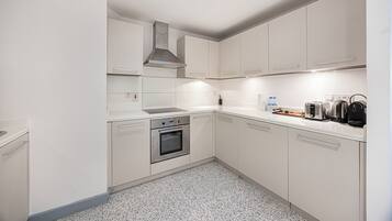 Een moderne keuken met witte kasten, roestvrijstalen apparatuur en een vloer met spikkeltjes.
