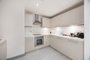 Een moderne keuken met witte kasten, roestvrijstalen apparatuur en een vloer met spikkeltjes.