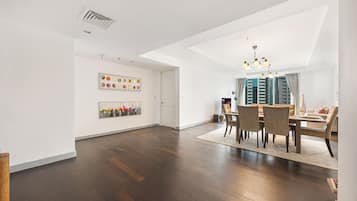 Een ruime eethoek met een moderne kroonluchter, een eettafel met stoelen en een uitzicht op hoge gebouwen door grote ramen.
