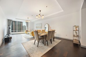 Un comedor moderno con techo alto, una mesa de comedor preparada para cuatro personas y un ventanal con vistas a edificios altos.