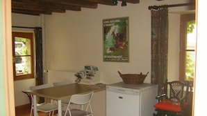 A small kitchen with a white refrigerator, a table with chairs, and a poster on the wall. - Holiday Home 'Les Grands Essarts' with Private Garden and Wi-Fi (Bagneaux)