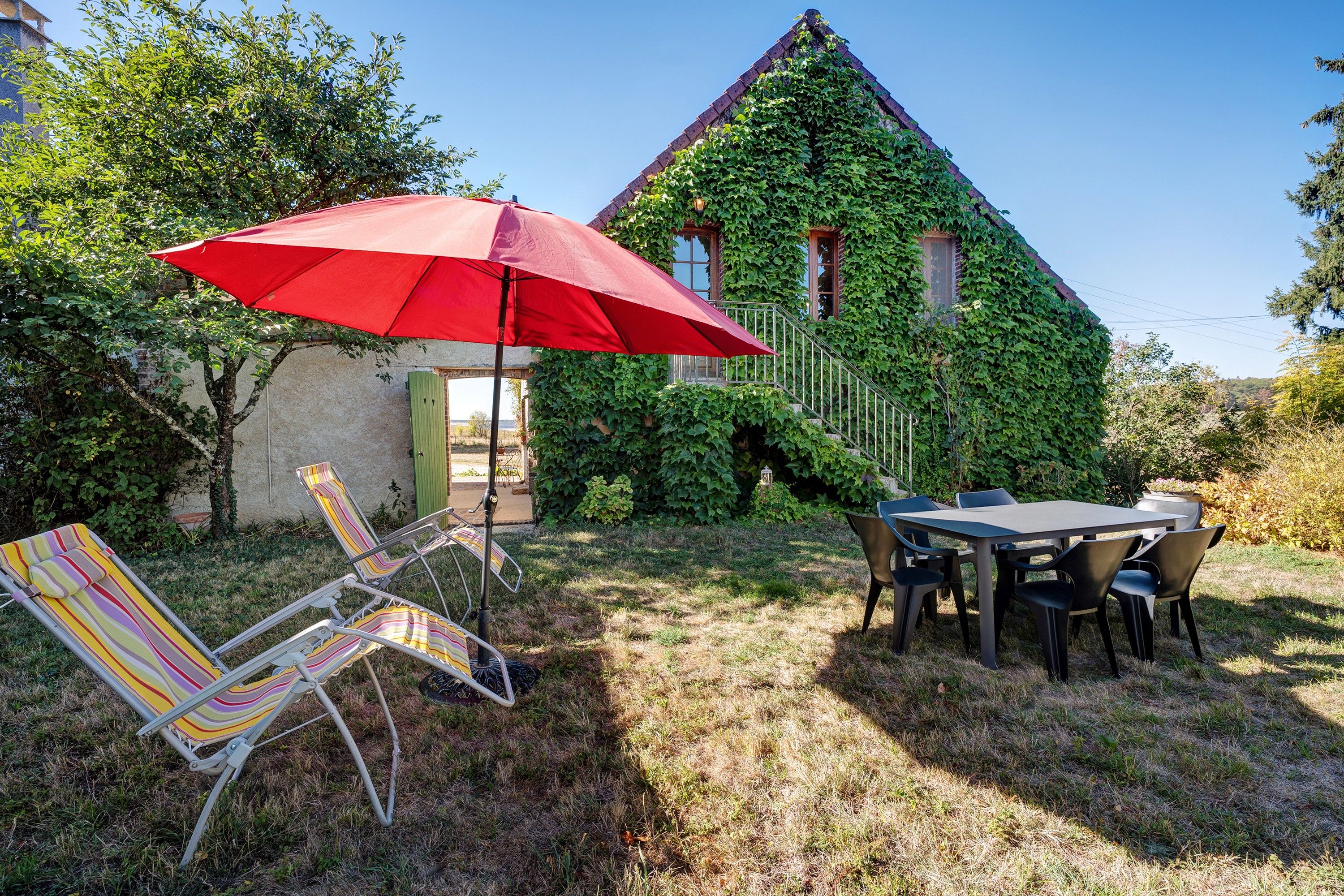 Un patio con una mesa y sillas, un paraguas rojo y una silla lounge a rayas.