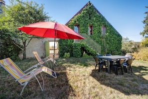 Une terrasse avec une table et des chaises, un parasol rouge et une chaise longue à rayures.