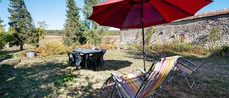 Eine Terrasse im Freien mit Tisch und Stühlen, einem roten Sonnenschirm und einem gestreiften Liegestuhl.