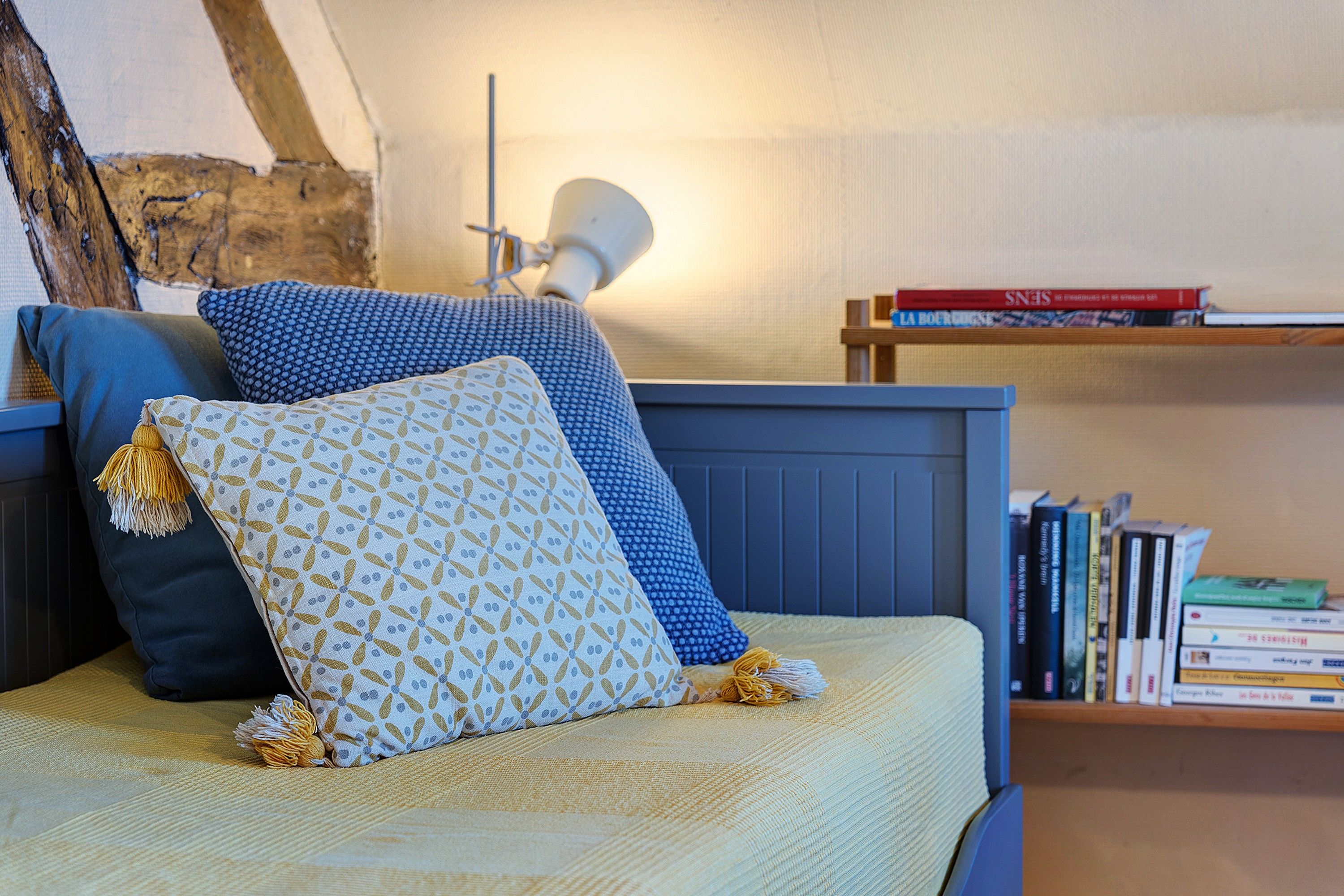 Una cama con almohadas estampadas, una lámpara de noche y una estantería con libros.