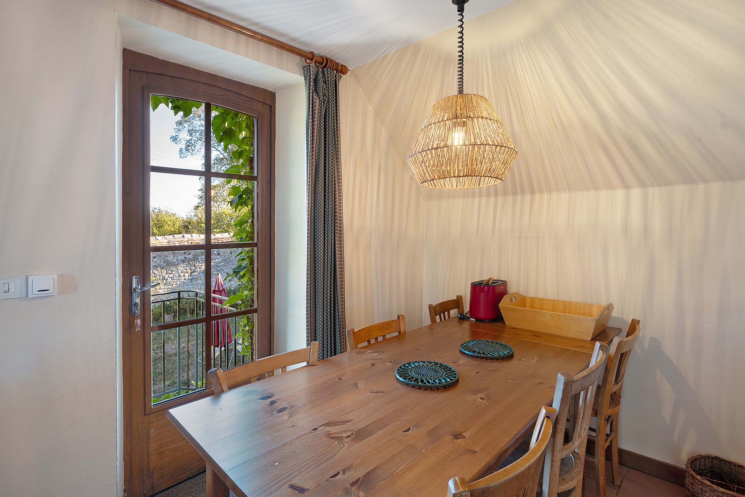 Un espace repas comprenant une table en bois, des chaises, un banc et un luminaire suspendu.