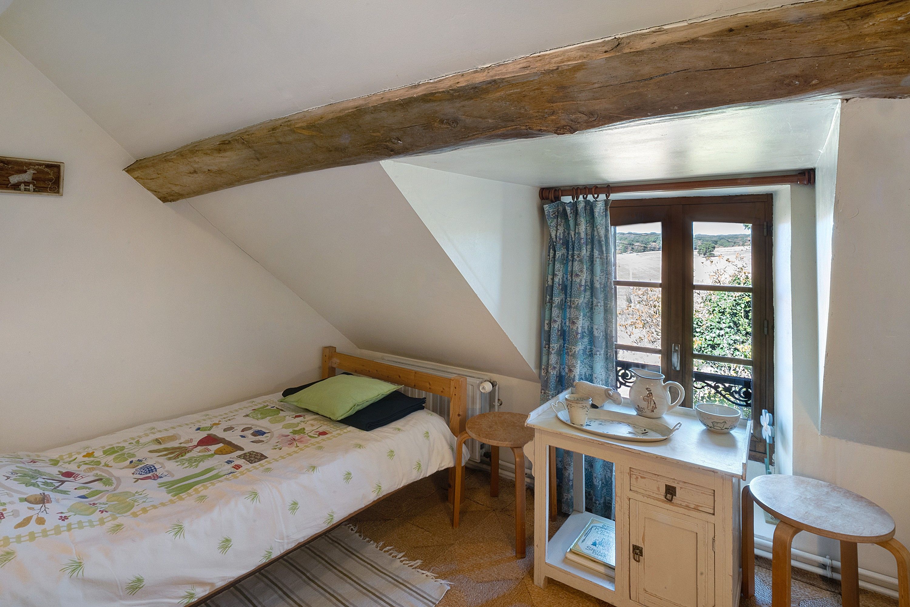 Een knus slaapkamer met een enkel bed, een houten bureau en een raam met gordijnen.