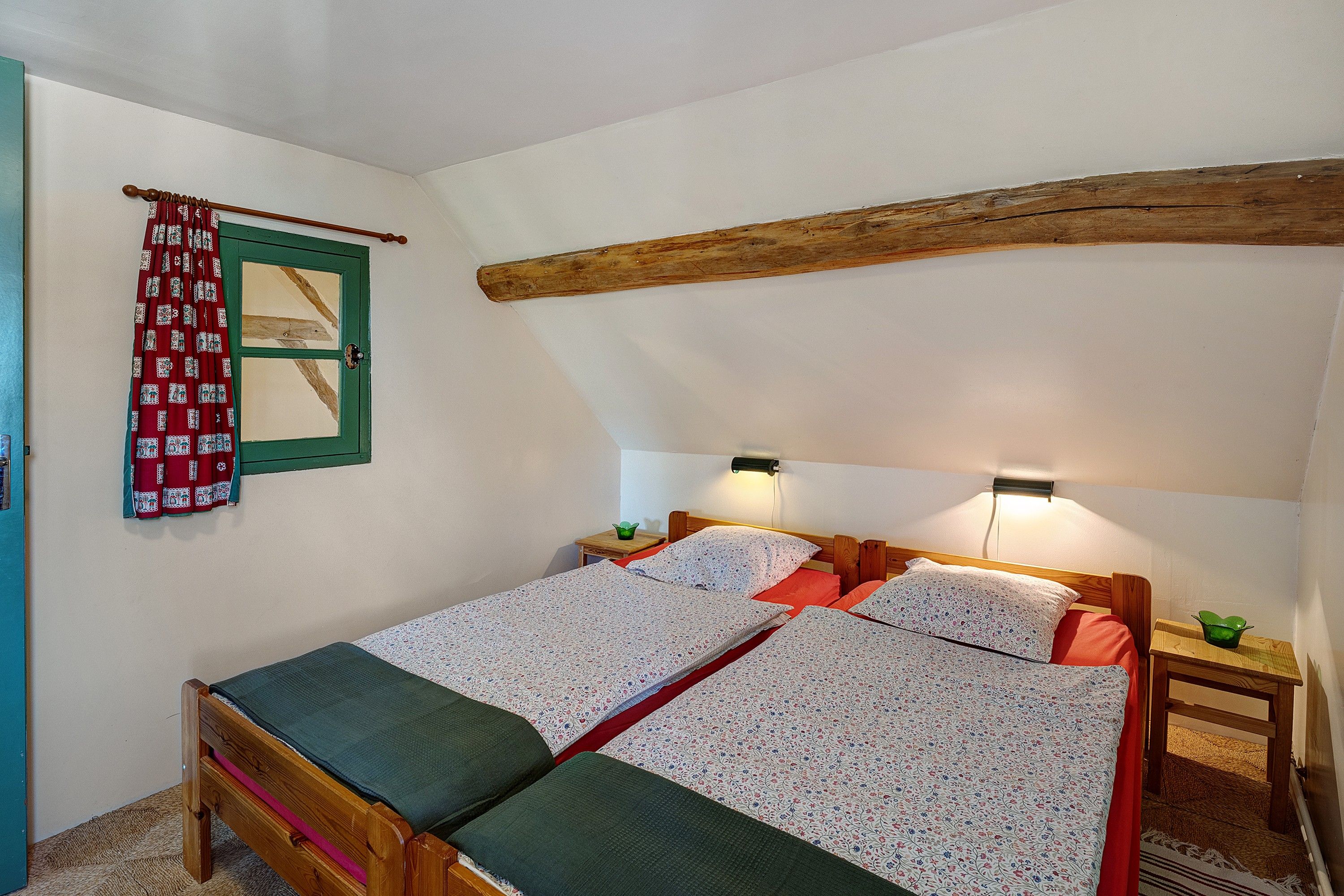A room with a wooden bed, a green door, and a small bedside table with a lamp.