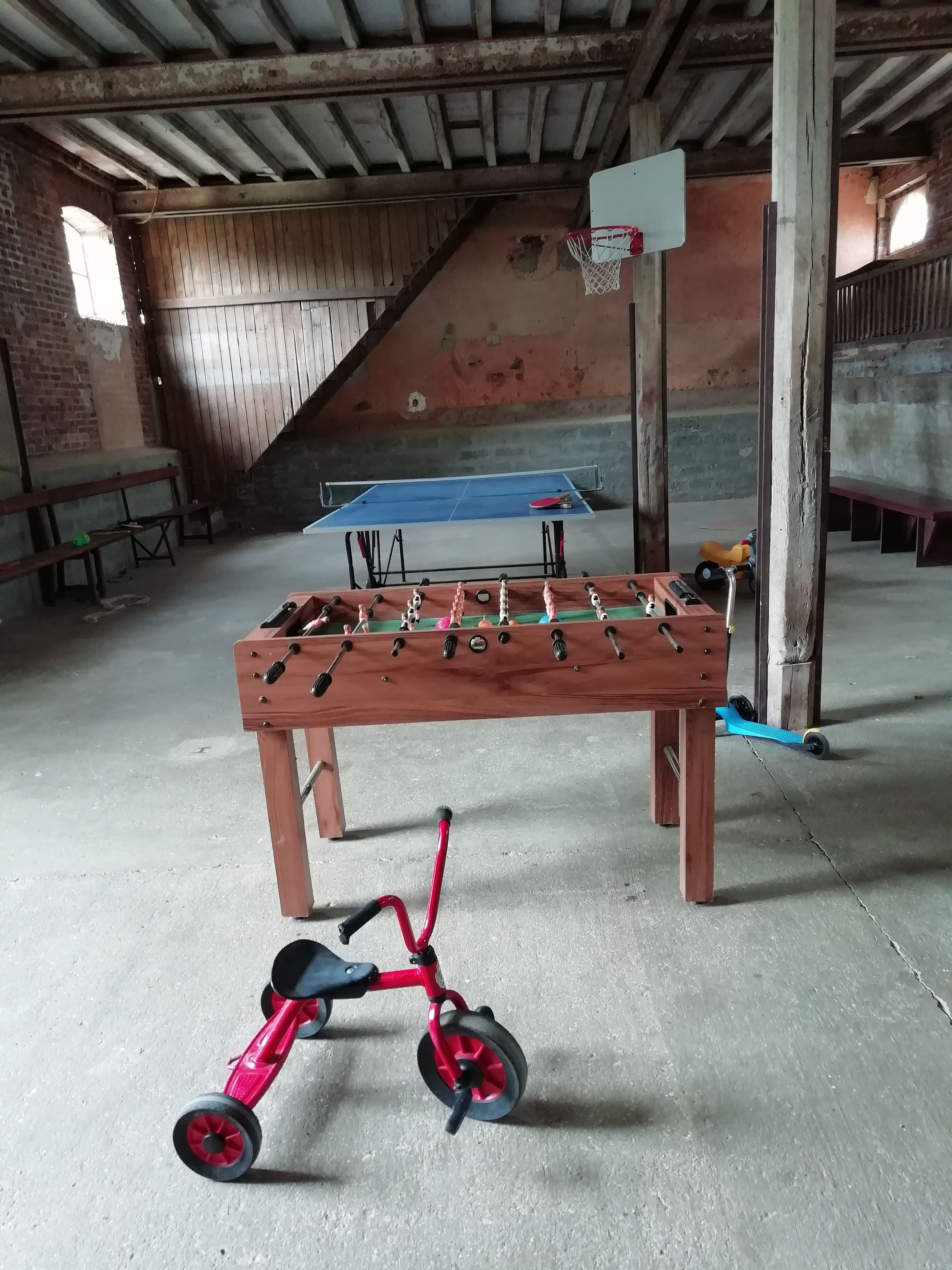 Ein Zimmer mit Tischfußball, Pong-Tisch und einem kleinen roten Dreirad.