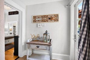 A hallway with a white door, a small table with a lantern, and a decorative wall piece. - Fire Pit, Grill, Smoker | 3 Min to Aquarium, 4 Min to Beach! (Gulfport)