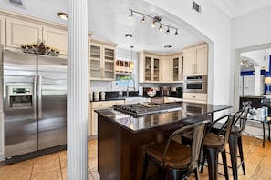 A modern kitchen with a central island, stainless steel appliances, and a dining area with bar stools. - Fire Pit, Grill, Smoker | 3 Min to Aquarium, 4 Min to Beach! (Gulfport)