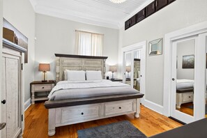 Ein Schlafzimmer mit einem großen Bett, zwei Nachttischen, einer Kommode, einem Spiegel und einer Deckenleuchte.